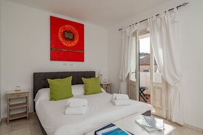 A bedroom with a bed, green pillows, white towels, a nightstand, a red artwork, and a view through a door. - Locanda Tartarughino - Suite Luna (Porto Rotondo)