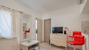 A room with a white vanity, a red chair, a television, and a mirror. - Locanda Tartarughino - Bilocale Sole (Porto Rotondo)