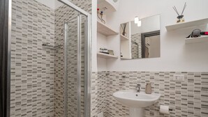 Une salle de bain avec une douche à parois de verre, un lavabo blanc et un mur recouvert de carreaux.
