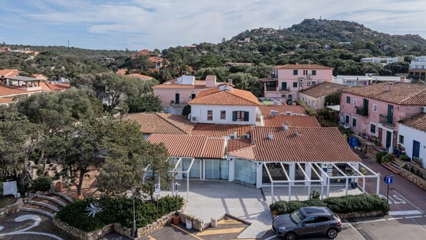 Un quartier résidentiel avec des maisons aux toits de tuiles, un bâtiment central doté d’une façade en verre et un paysage vallonné en arrière-plan.