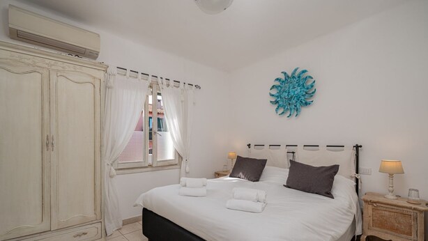 A bedroom with a large bed, a wardrobe, a window with curtains, a wall decoration, and bedside lamps.