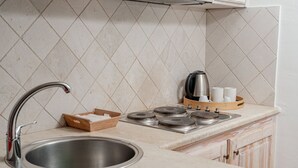 A kitchen with a stainless steel sink, a wooden cutting board, a kettle, and a tray with cups.