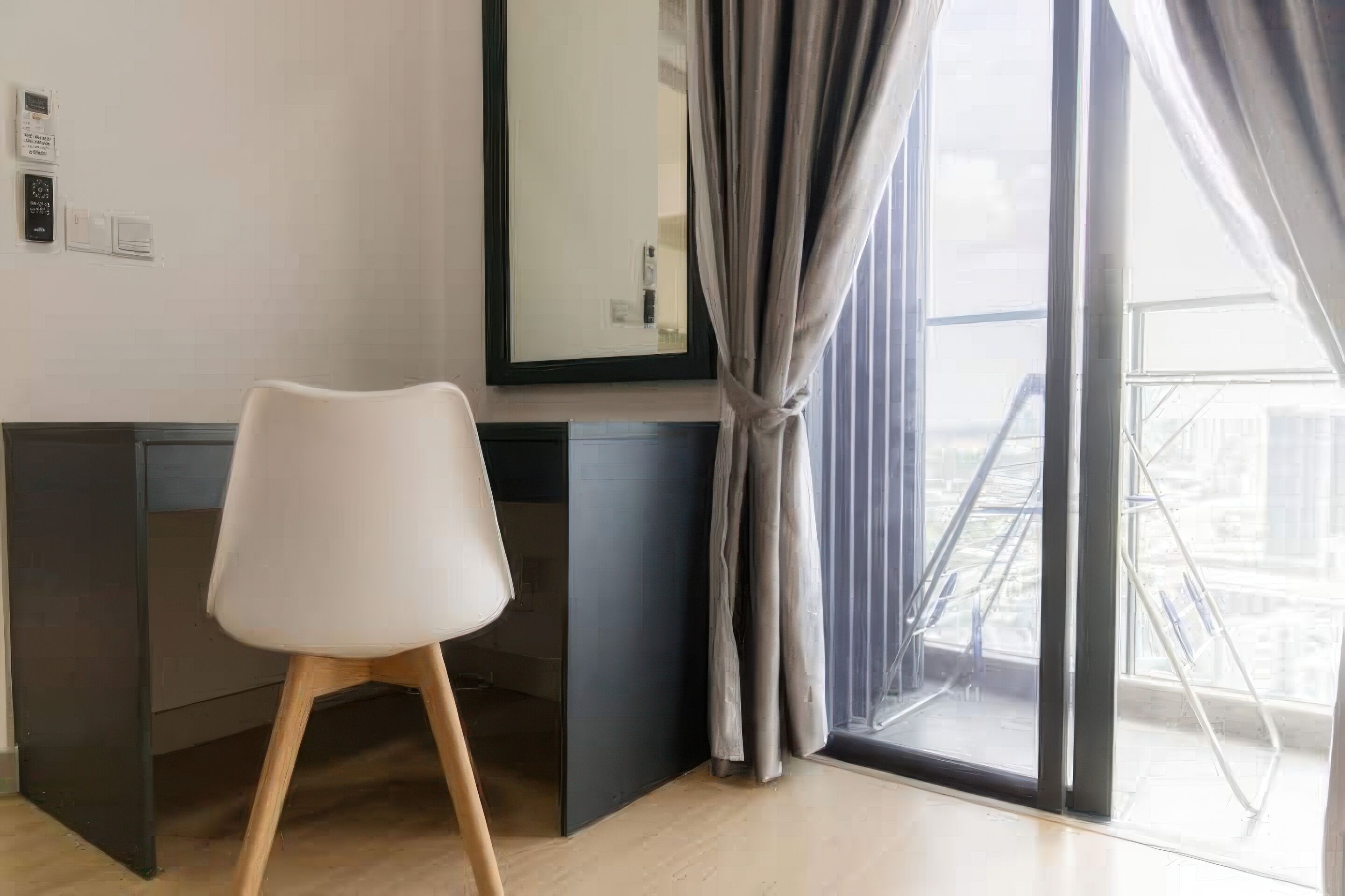 Una habitación moderna con una silla blanca, un escritorio oscuro y un amplio ventanal con cortinas.