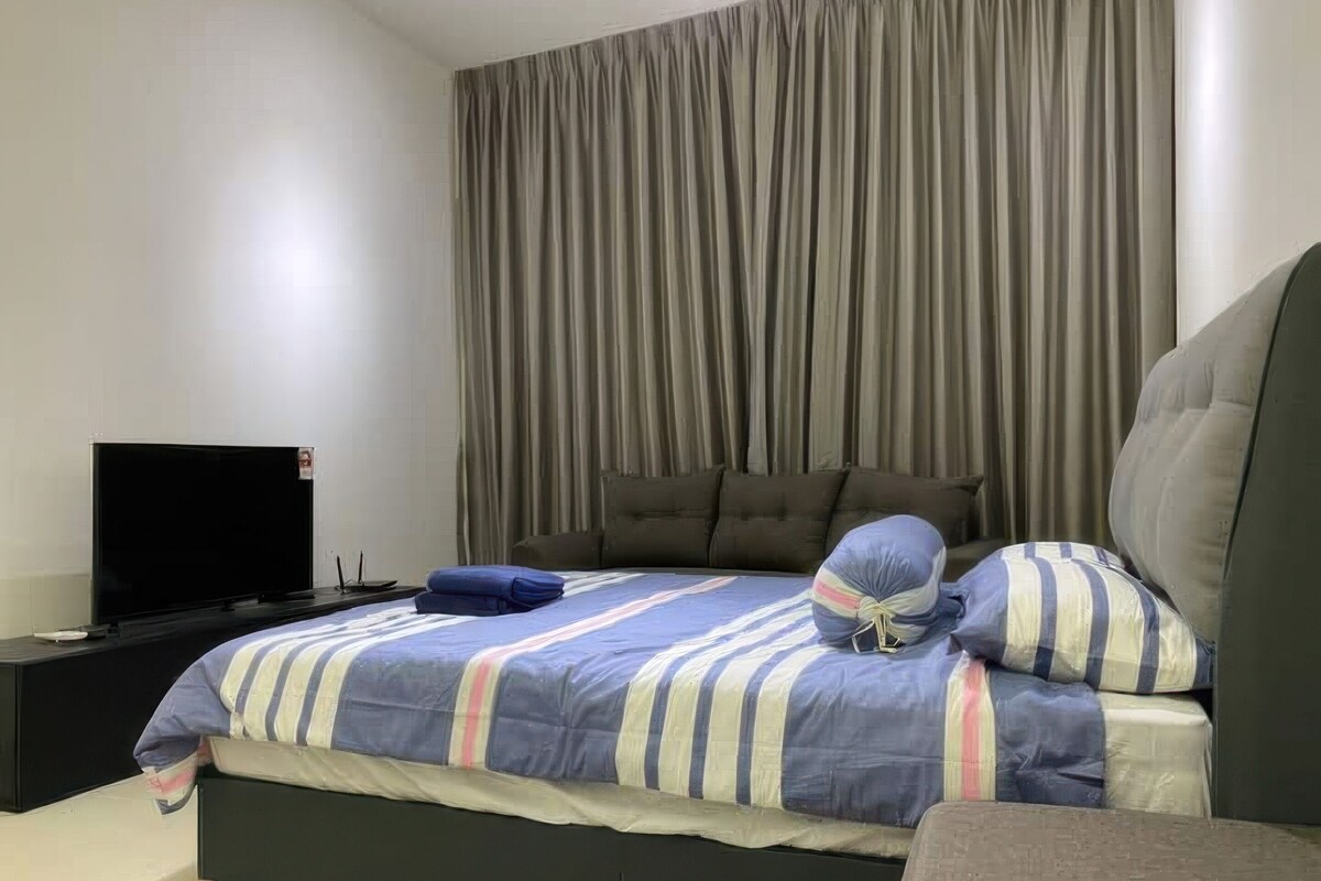 A bedroom with a bed, a flat-screen TV, a dark-colored nightstand, and a large window with curtains.