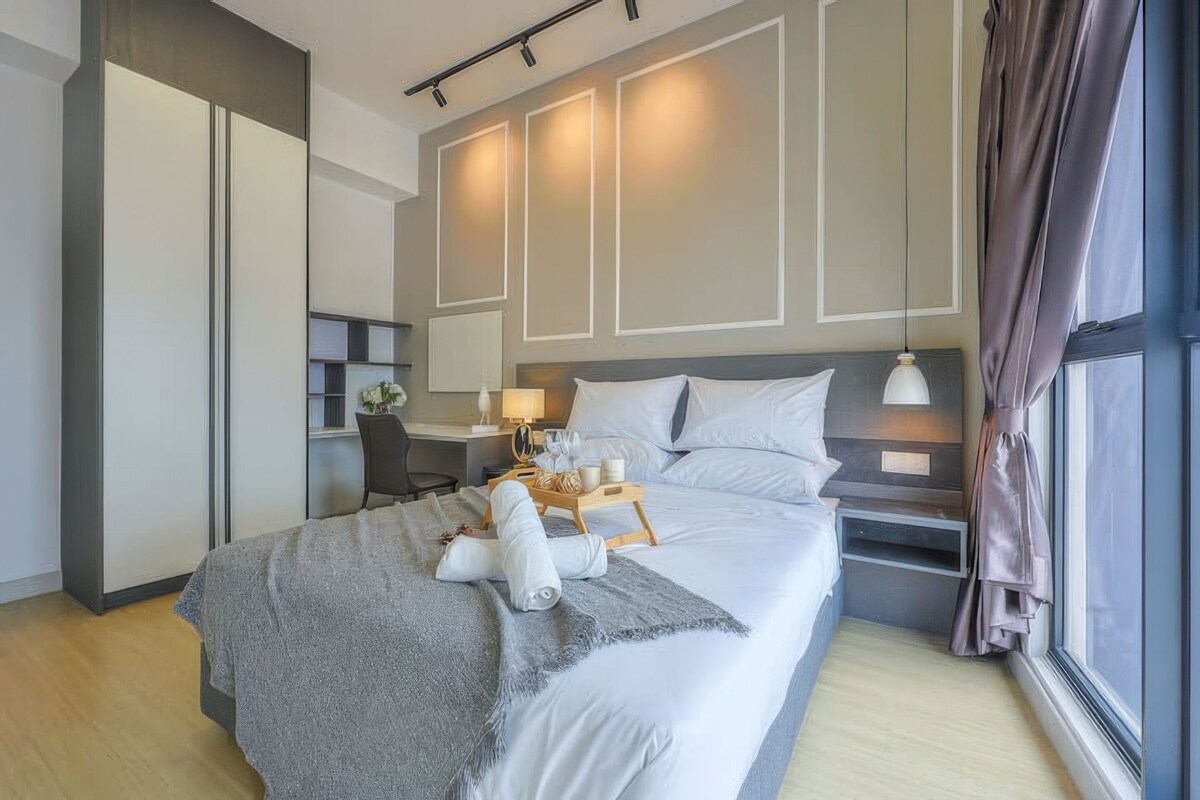 A modern hotel room with a large bed, bedside tables, a desk with a lamp, and a view of the outdoors.