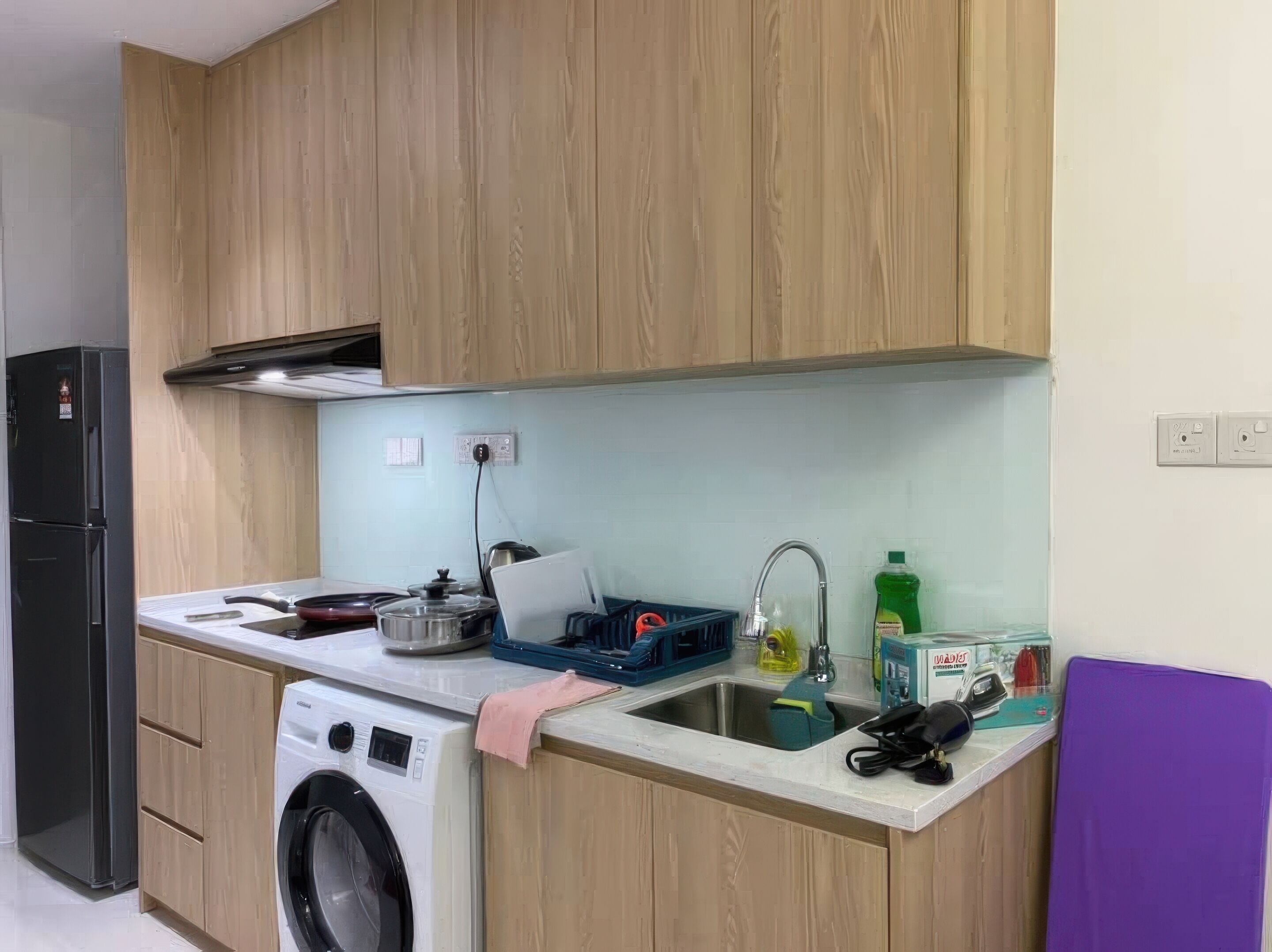 Een kleine keuken met houten kastjes, een wasmachine, een spoelbak en een koelkast.