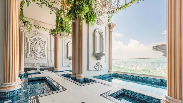 An indoor swimming pool with classical columns and decorative moldings, surrounded by a tiled floor with geometric patterns.