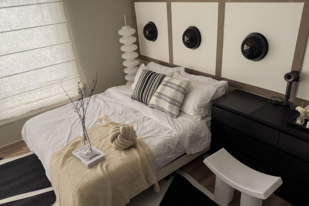 Une chambre à coucher moderne avec un lit, une table de chevet et un petit banc blanc.