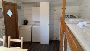 A compact room with a wooden door, a small kitchenette, a single bed, and a wooden table. - 4 Person Holiday Park Home in Rolfstorp (Rolfstorp)