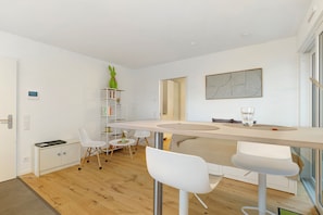Une cuisine moderne avec un plan de travail en bois, des chaises blanches et un objet décoratif vert posé sur une étagère.