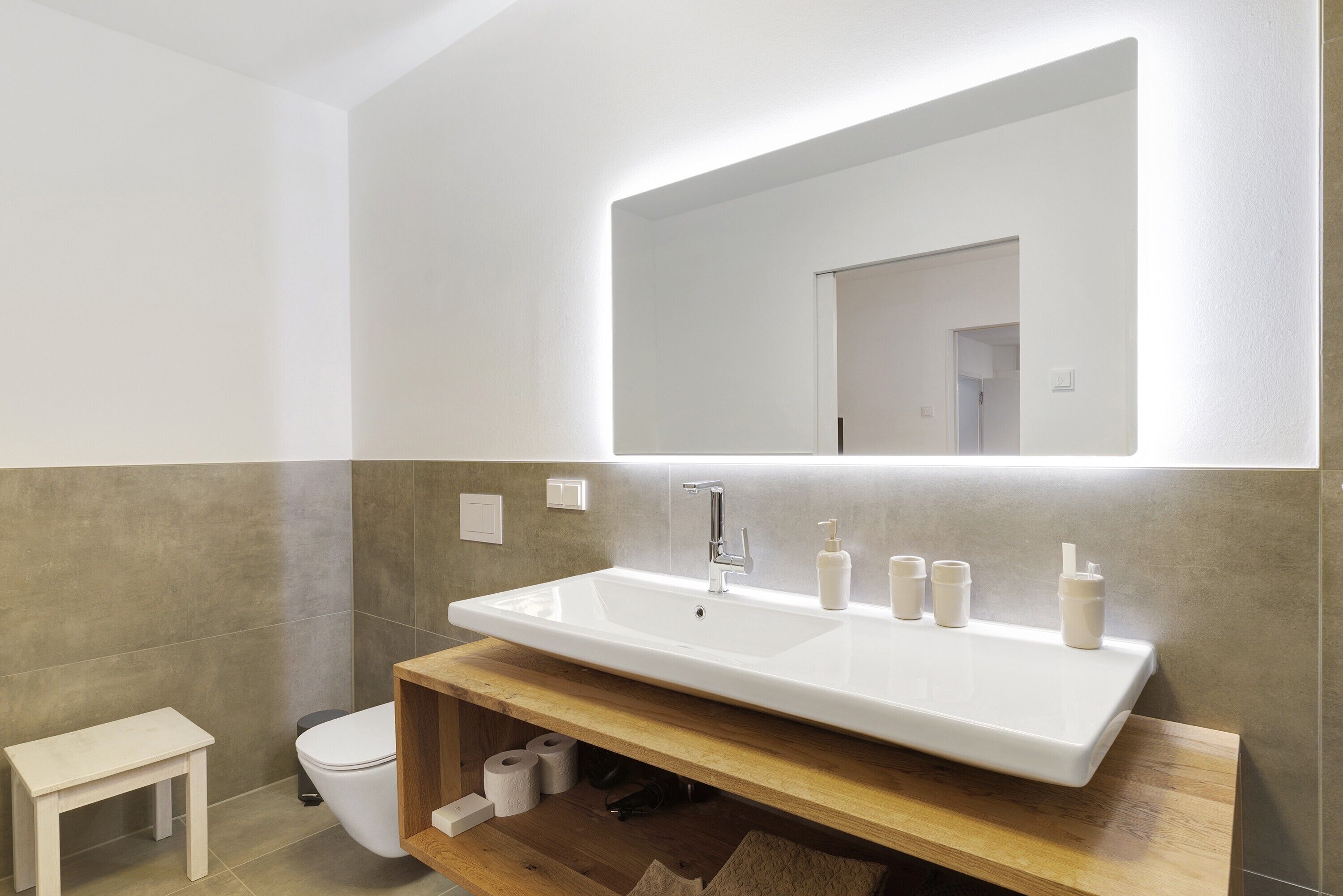 A modern bathroom with a large white sink, a mirror above it, and a wooden vanity.
