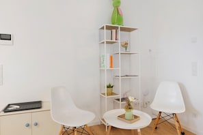 A room with two white chairs, a small round table, a white bookshelf, and a green decorative item on top.