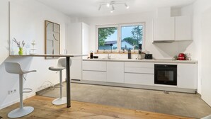 Een moderne keuken met witte kasten, een inbouwoven en een raam dat voor natuurlijk licht zorgt.