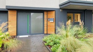 Een modern gebouw met een grijze gevel, een groene verticale accentuering en een houten lattenstructuur op de deuren.