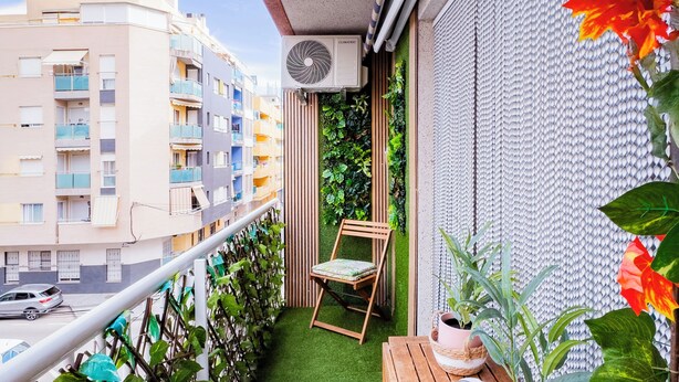 A balcony with artificial grass, a wooden chair, and potted plants.