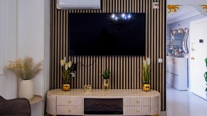 A modern living room with a flat-screen TV mounted on a wall with vertical stripes, a built-in entertainment unit below, and a small plant on the unit.