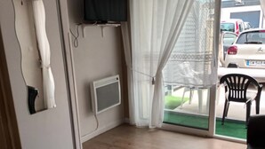 A room with a flat-screen TV mounted on the wall, a sliding glass door leading to an outdoor area with a car parked outside, and a wooden floor.