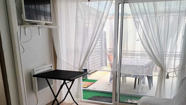 A room with a bed, a small table, a TV, and a sliding glass door to an outdoor area.