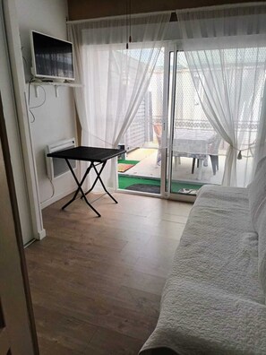 A room with a bed, a small table, a TV, and a sliding glass door to an outdoor area.