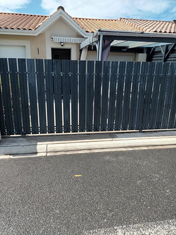 A residential area with a house featuring a tiled roof and a garage. A dark wooden fence runs along the front of the property.
