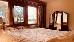 A bedroom with a large bed, wooden headboard, a window with curtains, and a mirror on the wall.