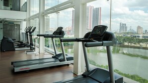A gym with treadmills and exercise equipment, large windows, and a view of a cityscape and river. - Zetapark Condominium by Emily in Town (Kuala Lumpur)