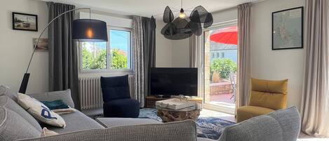 A living room with a sofa, a television, a lamp, and a view of the outdoors.