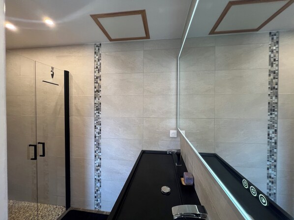 Un baño moderno con cabina de ducha de vidrio, encimera negra y pared de azulejos con detalle de mosaico.