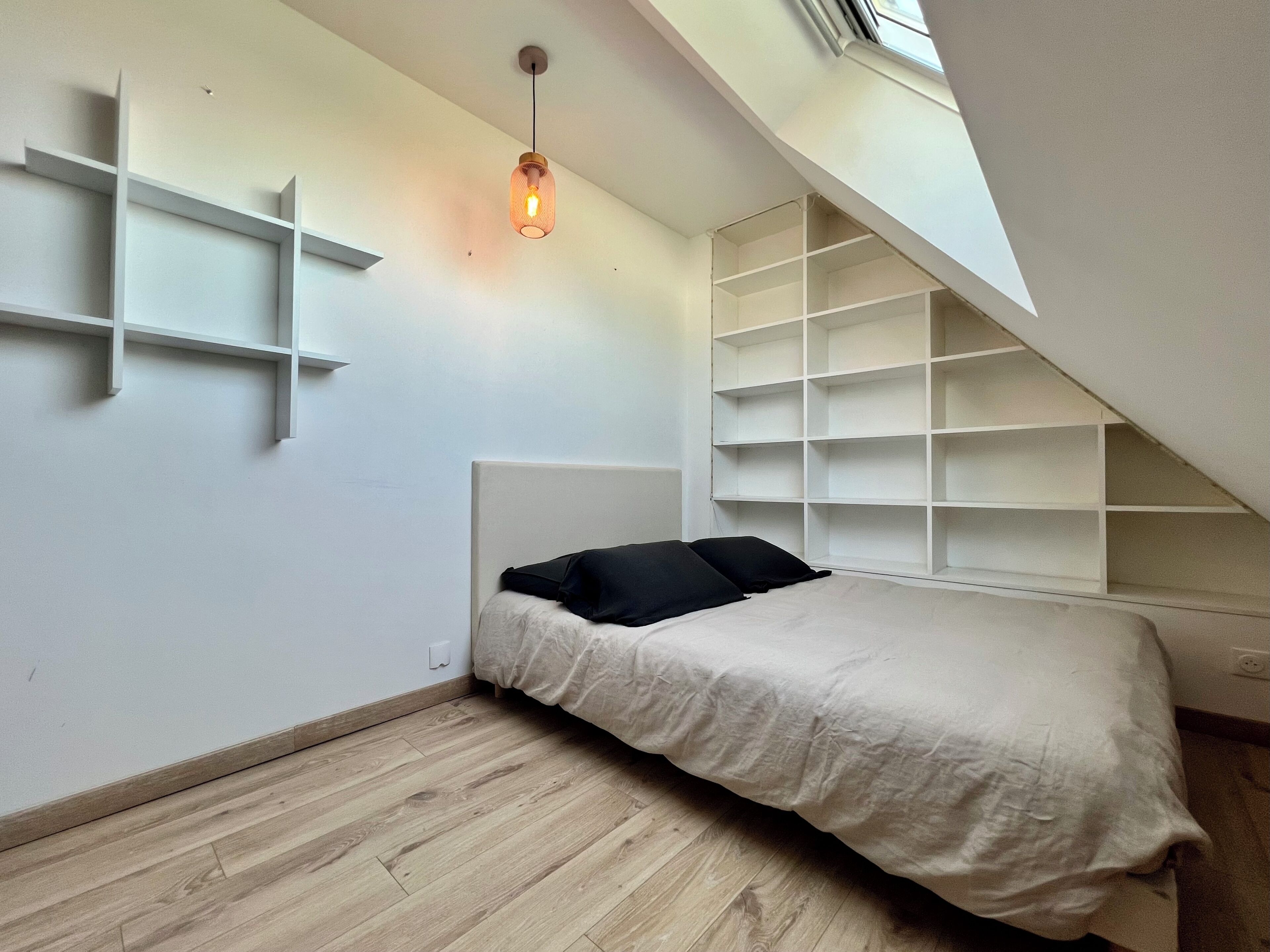 A small, modern bedroom with a sloped ceiling, a bed with black and white bedding, and a hanging light fixture.