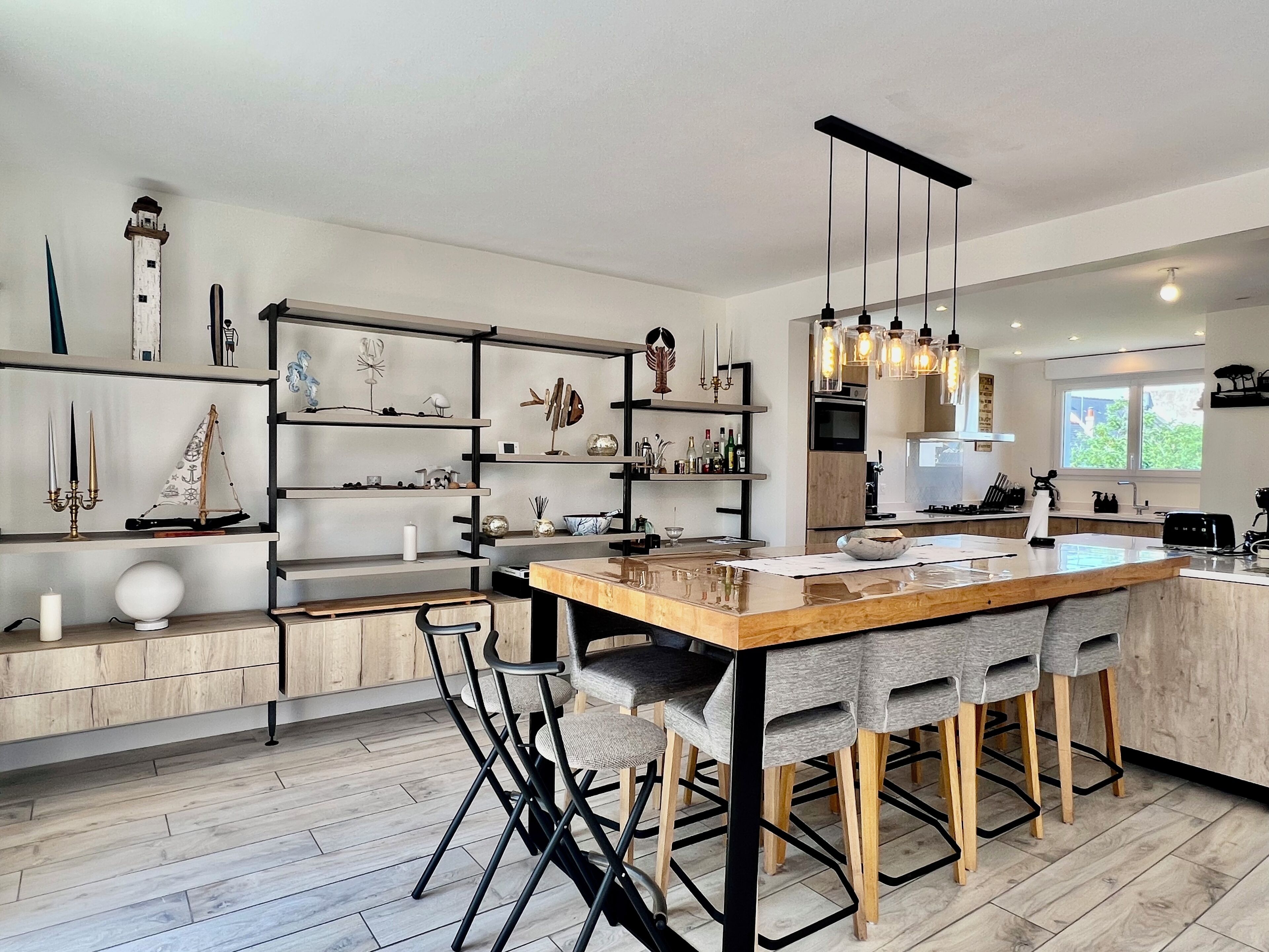 A modern kitchen with a central island, bar stools, and a variety of decorative items on shelves.