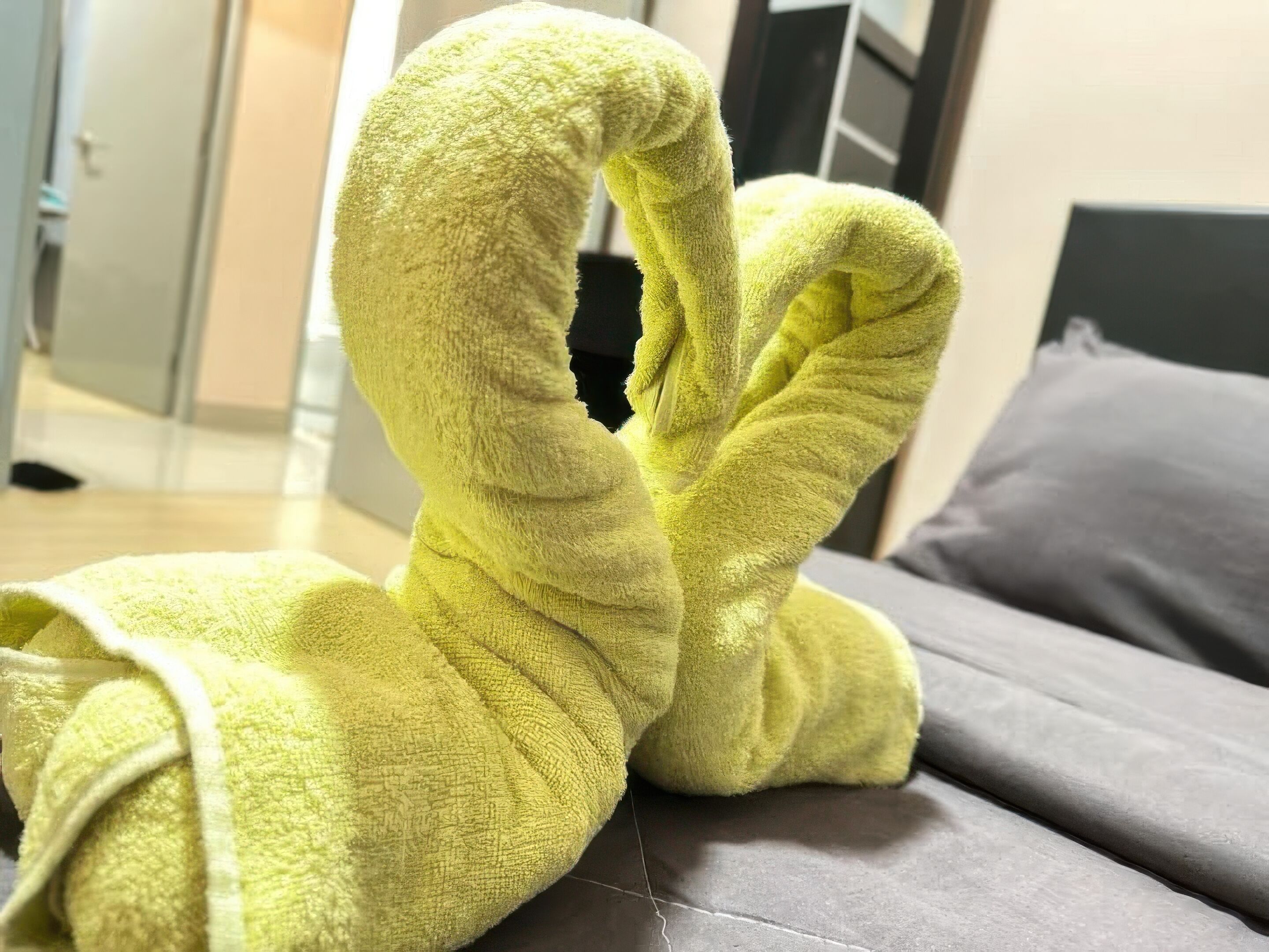 A bed with a grey mattress and a yellow towel folded in a heart shape.