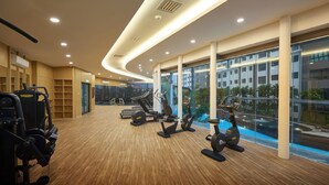 A modern gym with exercise equipment, large windows, and a view of the city.