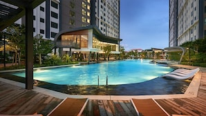 A modern hotel with a large swimming pool, lounge chairs, and a well-maintained garden area.