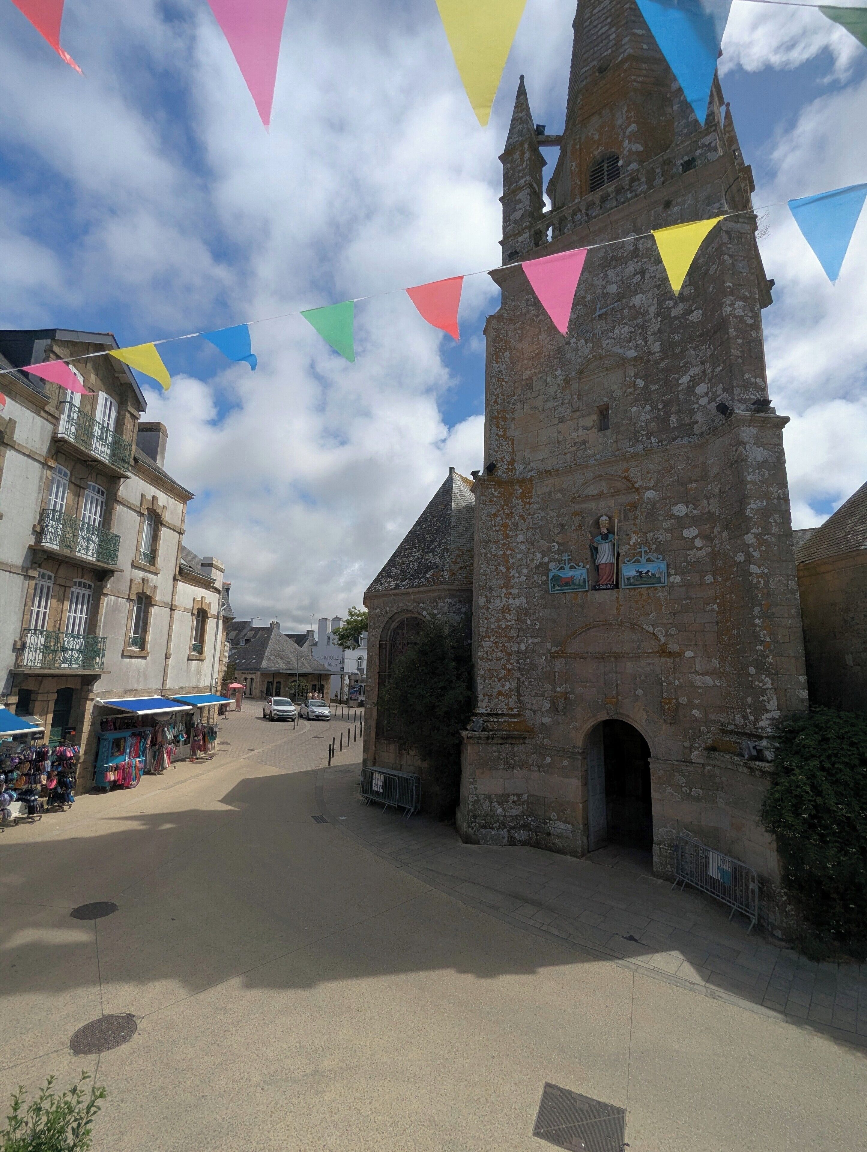 Ein historisches Steinhaus mit einem Turm, einem gepflasterten Platz und einem Markt mit Ständen.