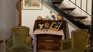 A staircase with a wooden handrail and metal balusters, flanked by two green upholstered chairs and a wooden chest of drawers with a cross and religious items. - The little house in the castle (Caso)