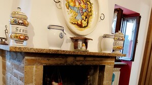 A fireplace with a stone mantle, a fruit bowl above it, and a rustic wooden chair. - The little house in the castle (Caso)