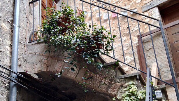 A narrow stone building with a metal balcony and a green door. - The little house in the castle (Caso)