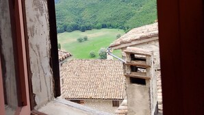 A view from a window overlooking a mountainous landscape with a rustic building in the foreground. - The little house in the castle (Caso)