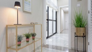 A hallway with a wooden console table holding potted plants, a floor lamp, and a large window with blinds. - Genteel Home Plaza de las Tendillas (Córdoba)