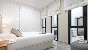 A modern bedroom with a large bed, a wooden nightstand, a grey armchair, and a view of the outside through a glass door. - Genteel Home Plaza de las Tendillas (Córdoba)