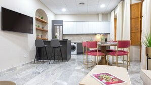 A modern kitchen with white cabinets, a flat-screen TV, and a dining area with a table and chairs. - Genteel Home Plaza de las Tendillas (Córdoba)