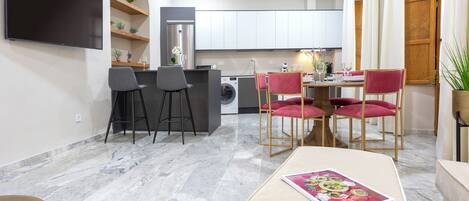 Una cocina moderna con armarios blancos, un televisor de pantalla plana y un comedor con mesa y sillas.