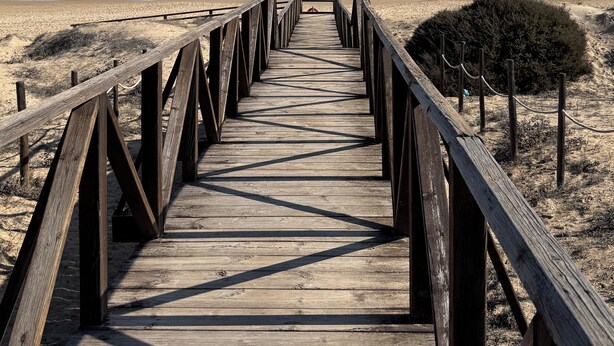 A wooden boardwalk leading to a beach with a clear view of the ocean.