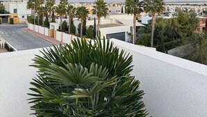 A rooftop terrace with a view of a cityscape at sunset, featuring palm trees and modern buildings.