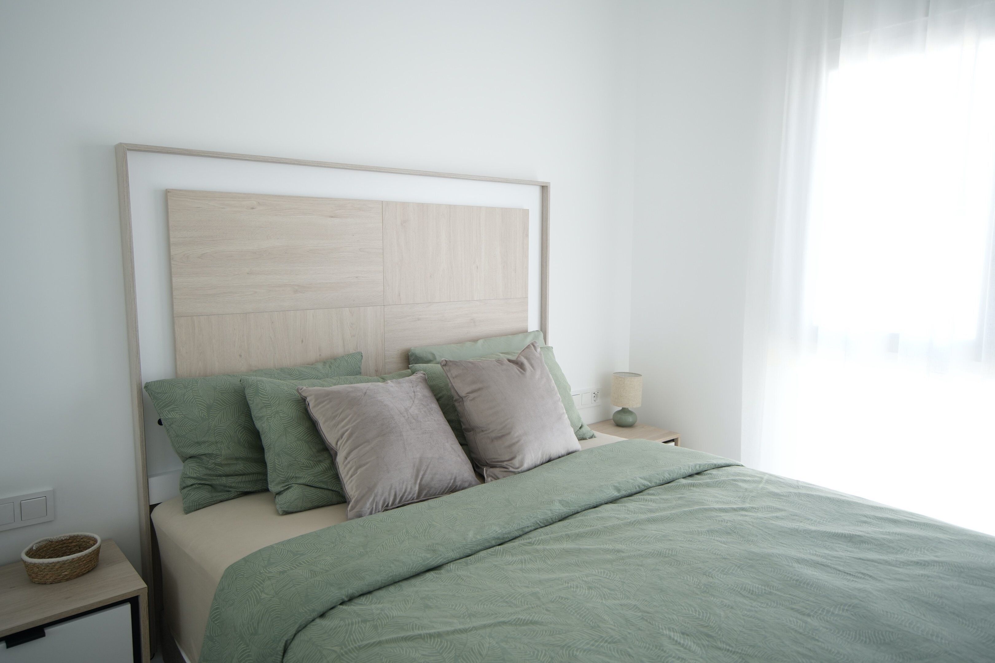 A neatly made bed with a light-colored headboard, two pillows, and a green blanket.