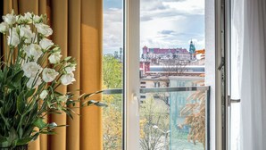 Une pièce dotée d’une grande fenêtre, d’un bouquet de fleurs blanches et offrant une vue sur un paysage urbain avec des bâtiments et des arbres.