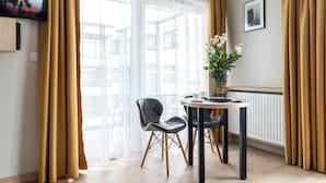 Un salon moderne avec un coin repas, comprenant un téléviseur fixé au mur, une table à manger avec des chaises et une grande fenêtre agrémentée de rideaux légers.