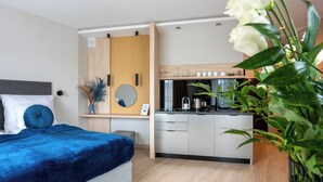 Une chambre d’hôtel moderne équipée d’un lit, d’une table de chevet, d’un miroir et d’un coin cuisine.