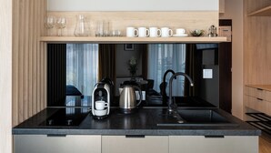 Une cuisine moderne avec un plan de travail noir, des appareils en acier inoxydable et une étagère en bois au-dessus de l’évier.