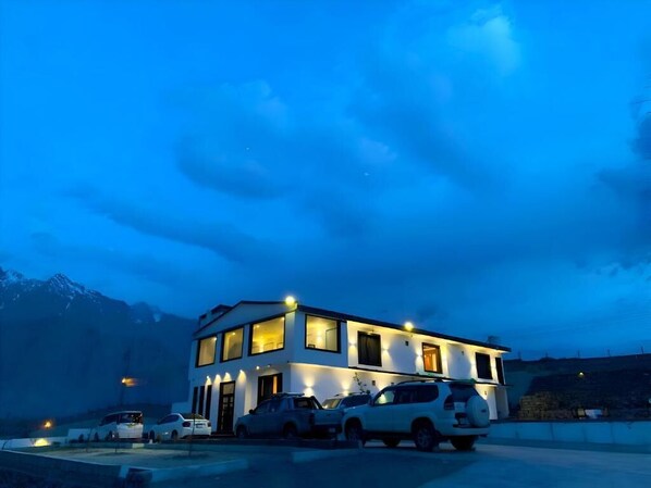 A modern two-story building with a parking area in front, surrounded by mountains. - Starlit Hotel Skardu (Skardu)